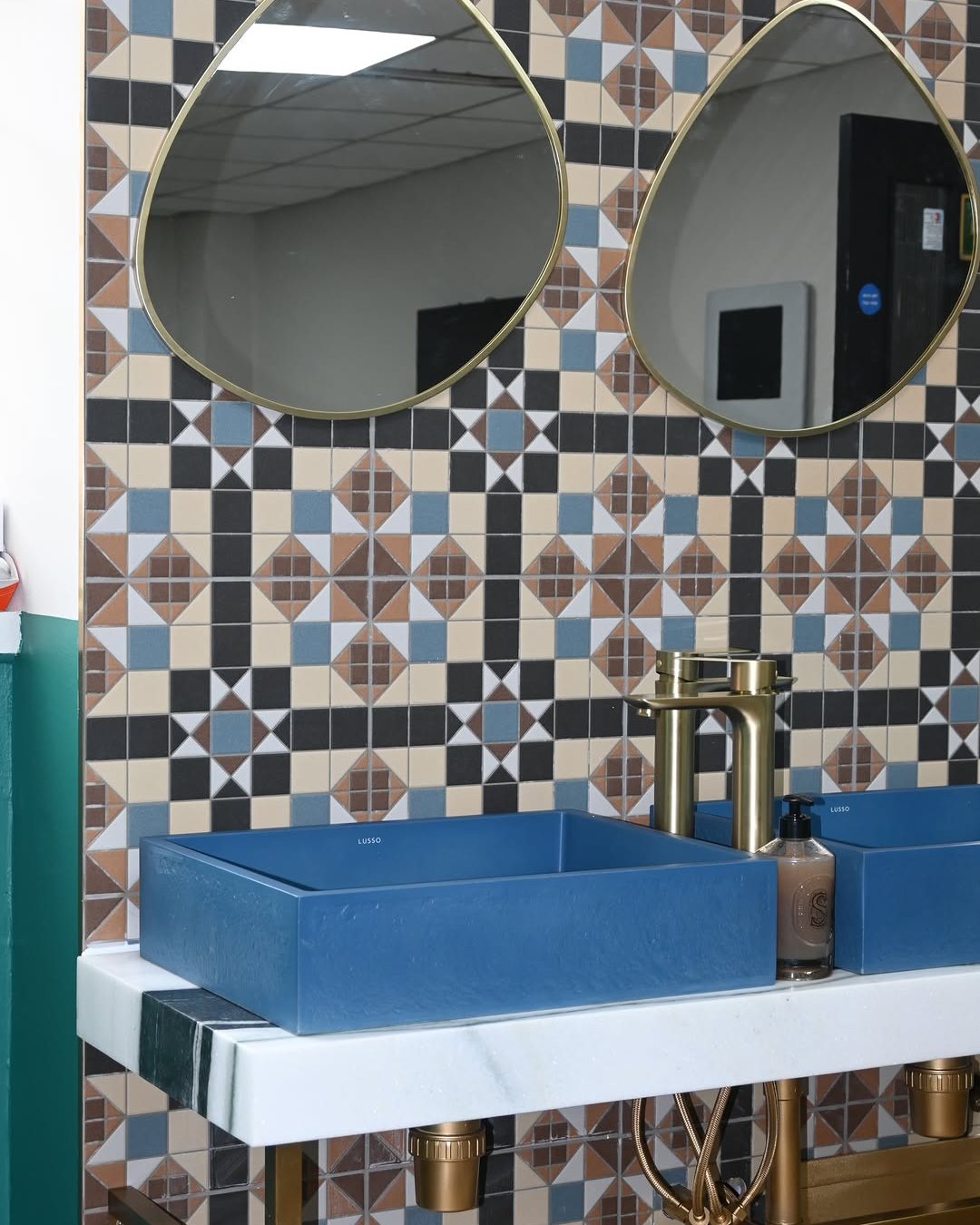 The washroom at ASK Wellness, with patterned tiles, blue basins and brass taps