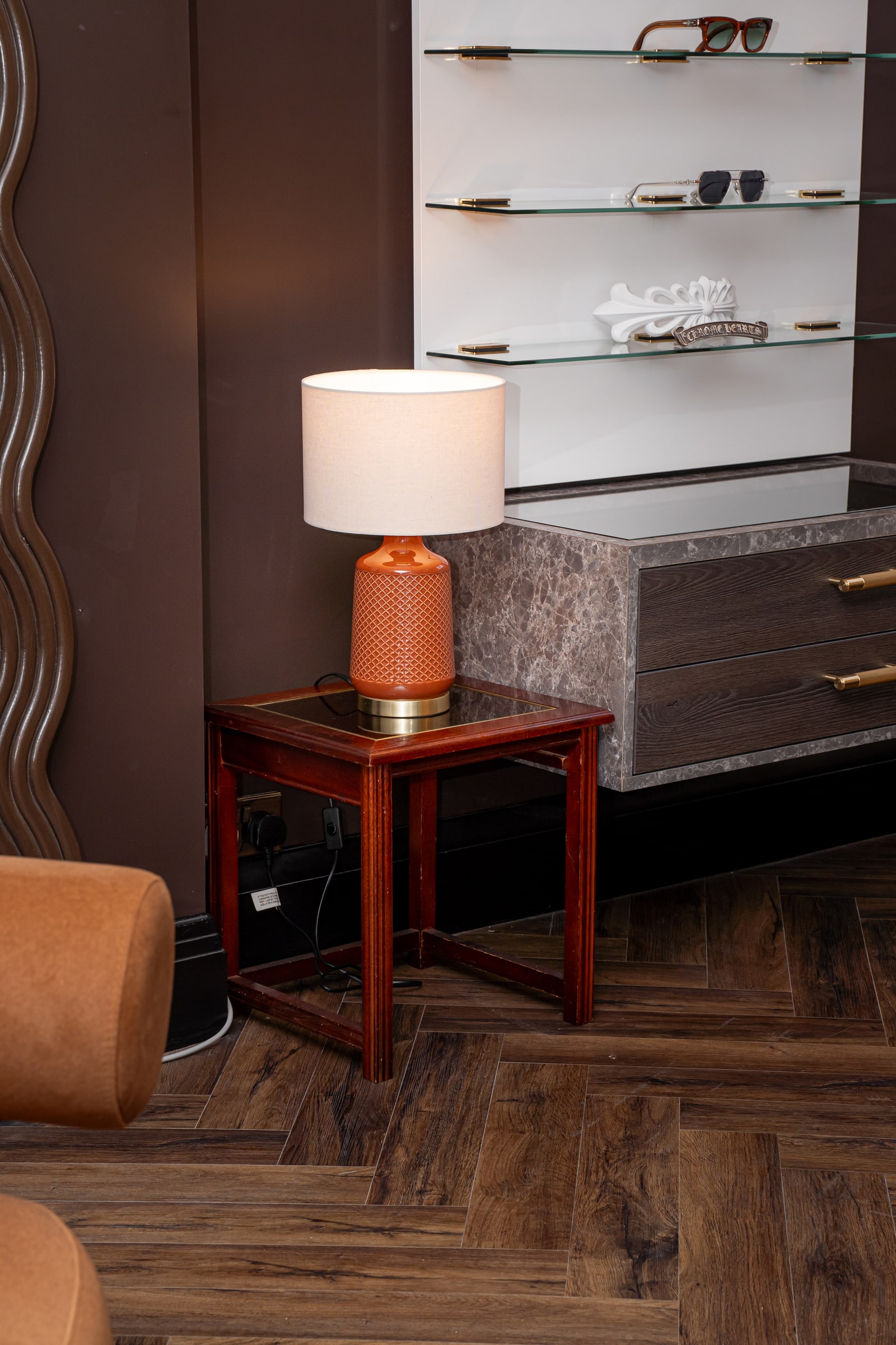 A warm table lamp beside the lounge and illuminated eyewear shelves