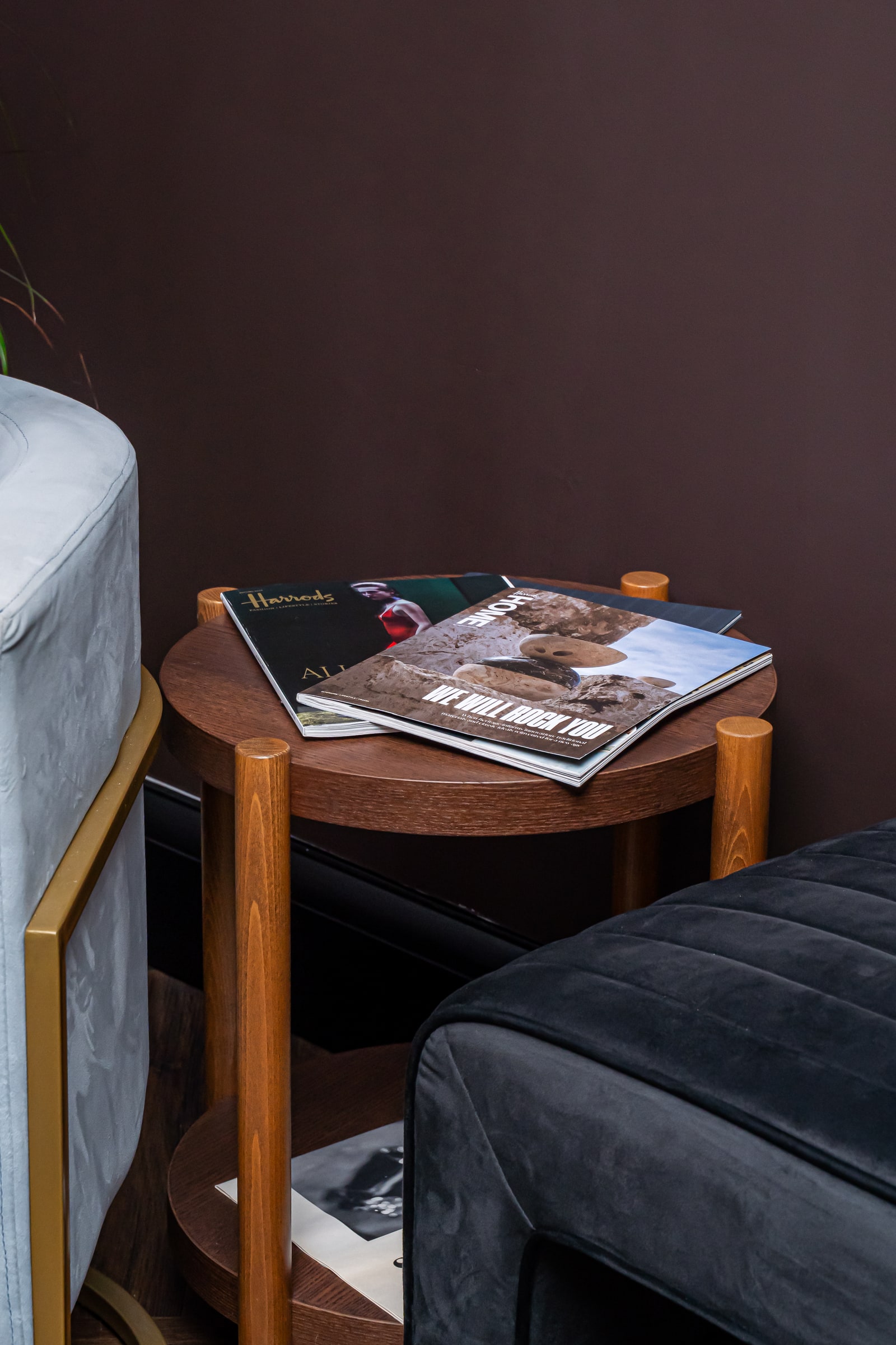 A side table with magazines beside the blue velvet lounge chair
