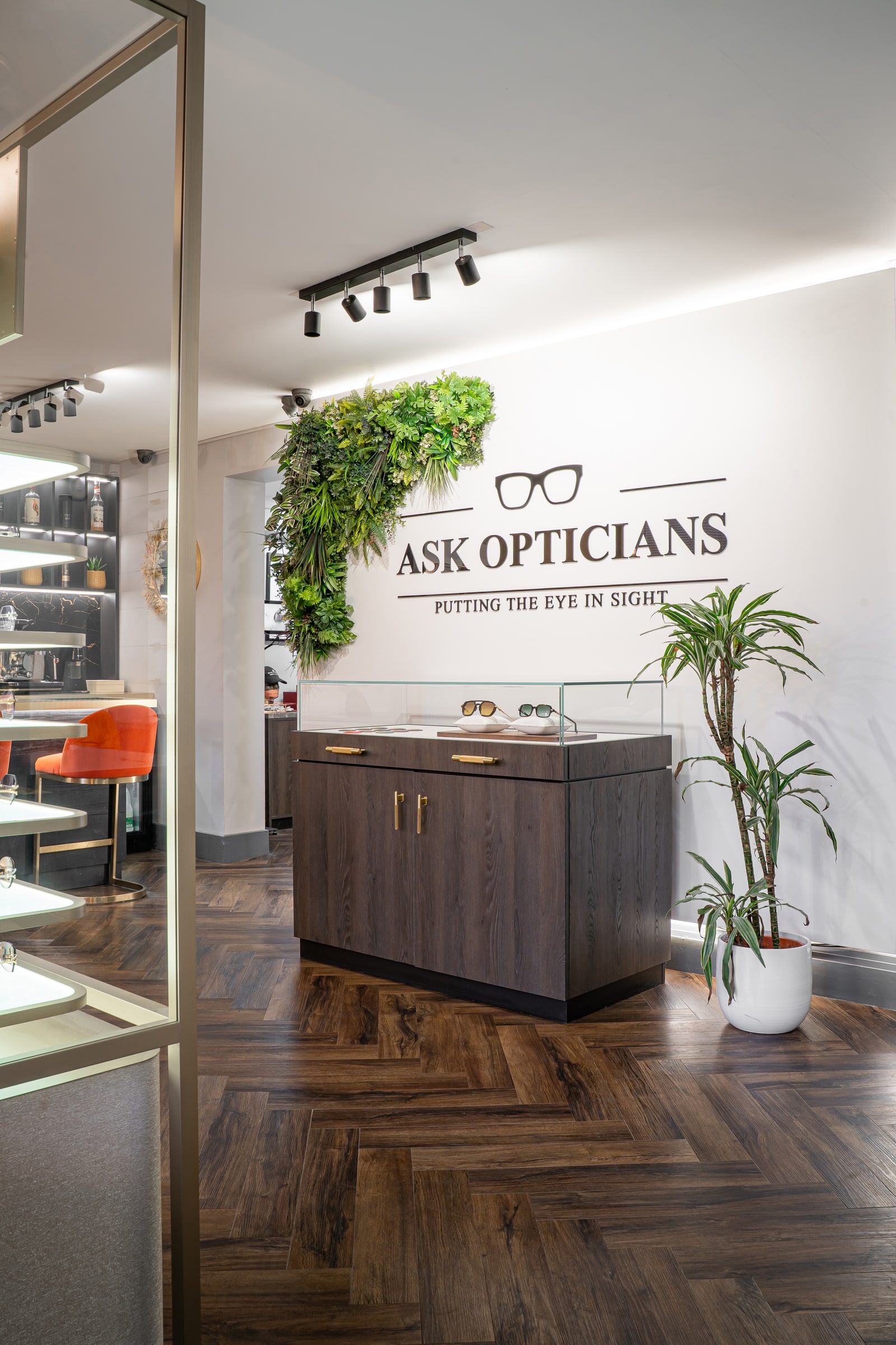 The ASK Opticians sign above a display cabinet, with plants and the bar beyond