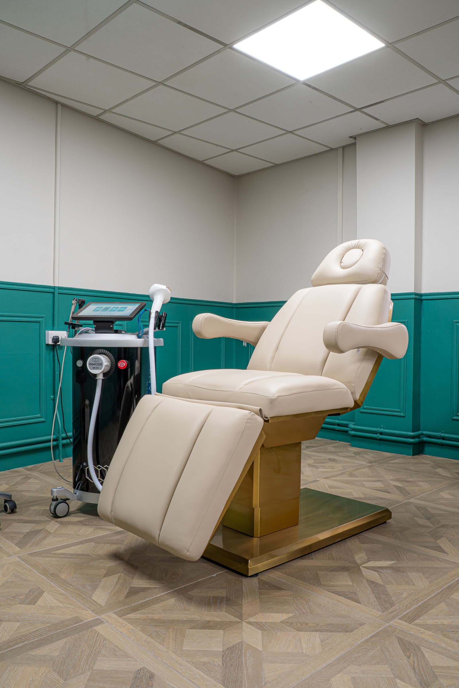 The cream treatment chair and InMode equipment in the green-panelled wellness room