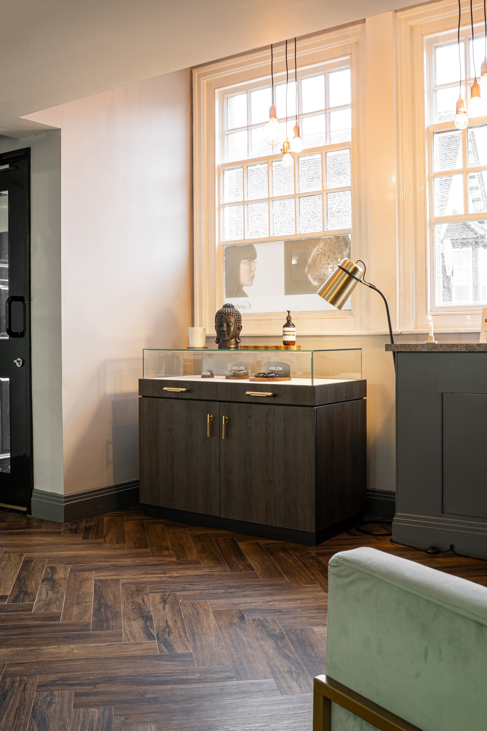 The glass eyewear cabinet and brass lamp beside the front window